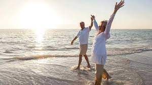 A happy couple enjoying a seaside stroll, with arms raised in celebration as the sun sets over the horizon, enjoying their Retirement in Langebaan