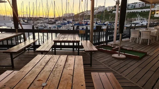 The wooden deck of the Kapstadt Brauhaus in Langebaan with wooden table and seating looking onto the Marina with yachts, at Club Mykonos