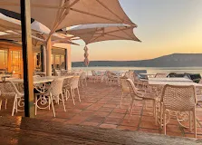 The outside eating area of La petite Restaurant in Langebaan at the Farmhouse hotel, with white chairs, tables and umbrellas with great view over the lagoon at sunset