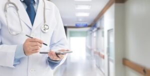 A Doctor, dressed in white over coat and blue tie, makes notes with pen and notepad in a hospital to provide better Medical Care in Langebaan