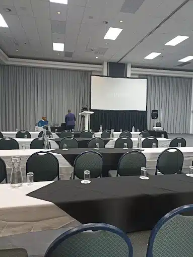 People setting up conference facility at Athene Conference Centre in Langebaan with big screen, tables and chairs in blue and white linen.