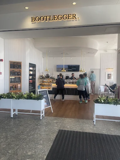 People standing in front of serving counter of Bootlegger Coffee Shop in Langebaan. Wooden floors with white flower boxes and neon signage are visible.