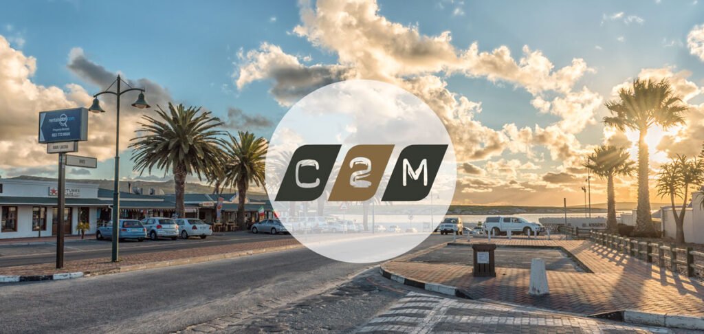 A picture of Bree Street in Langebaan with all the shops down Bree Street towards the lagoon, with the logo of C2M Chartered Accountants in a circle, in the middle.of the picture.