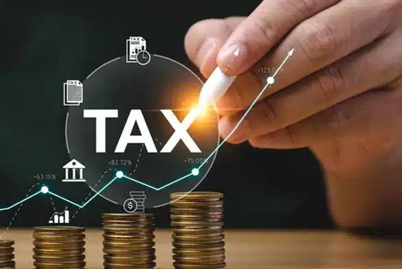 Money coins pilled up to indicated growth while a hand is pointing with white pen at Tax letters in white with dark background. This indicates the service that C2M Chartered Accountants in Langebaan can provide.