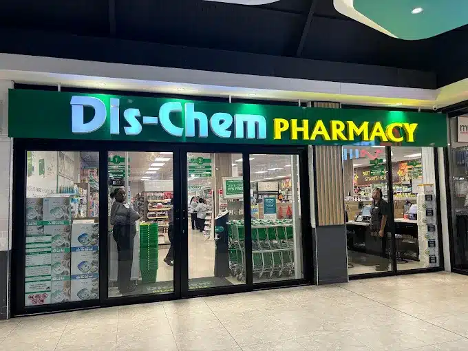Bold neon signage of Dis-Chem Pharmacy, shining on a green background, on top of glass doors that provides access to the Pharmacy in the Laguna Mall in Langebaan.
