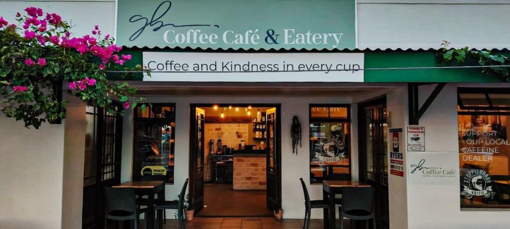 The front entrance to Ginja Beanz Coffee Cafe in Langebaan with green canopy, signage on the roof and wall and tables and chairs outside under canopy of this Coffee Shop.