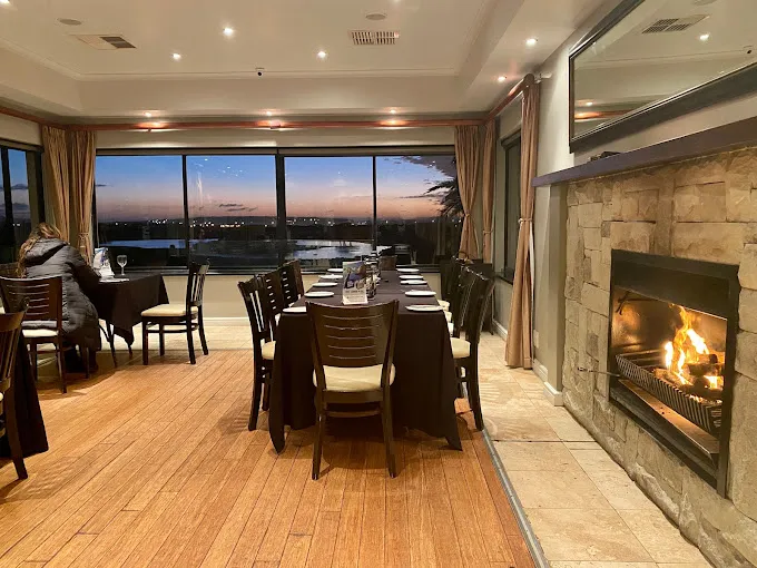 Wooden floors, burning fireplace, dark tables and chairs with window onto golf course, enjoyying the sunset over the lagoon at Horizon Restaurant in Langebaan.