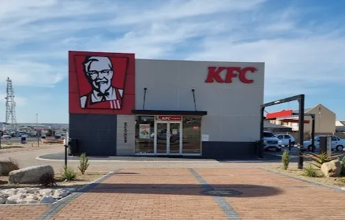 Outside view towards the building of KFC in Langebaan, with pavedd drive through, glass front entrance and massive promotional signage in red on the building.