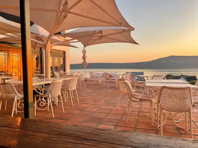 At Sunset on the deck outside the La Petite Restaurant at the Farmhouse Hotel in Langebaan. Seating around tables with white umbrellas with a great view over the lagoon.