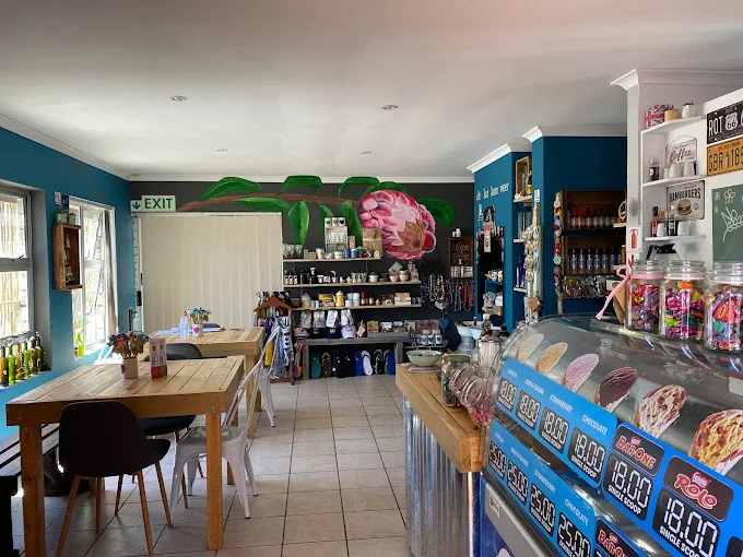 The innterior Die Kyjirhys Langebaan Coffee Shop with blue serving counter, wooden table and chairs and lots of home made merchandise on display.