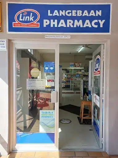 The entrance to the Langebaan Link Pharmacy with glass doors, bright blue signage above door and display cabinets visible inside the Pharmacy.