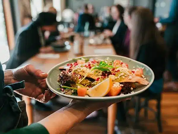 A Waiter carries a plate of food to waiting customers at a table at Restaurants in Langebaan