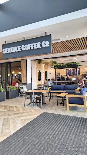 White signage on a dark board hangs from the ceiling at the entrance to Seattle Coffee Company in Langebaan with lots of seating options around wooden tables and blue covered cushions.