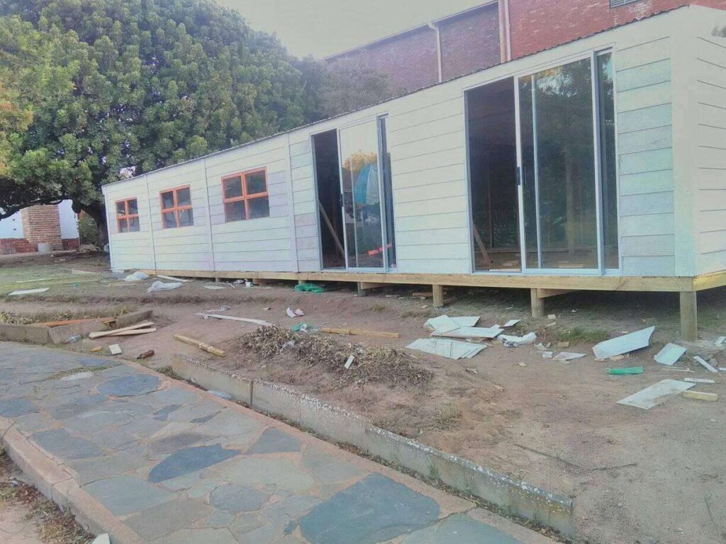 A nearly completed Wendy house in length showing sliding doors, wooden windows and white exterior paint by Laguna Wendy's in Langebaan with building material still lying around next to stoned payment.