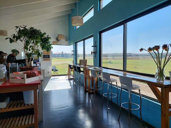 Lots of glass windows with a view on the golf course with seating in front of them, all in white at Soldato Cafe in Langebaan.