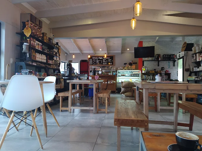 The interior of Weskus Coffee Roastery in Langebaan with different seating options at wooden tables, white chairs and serving counter and shelves with goods, in a distance.