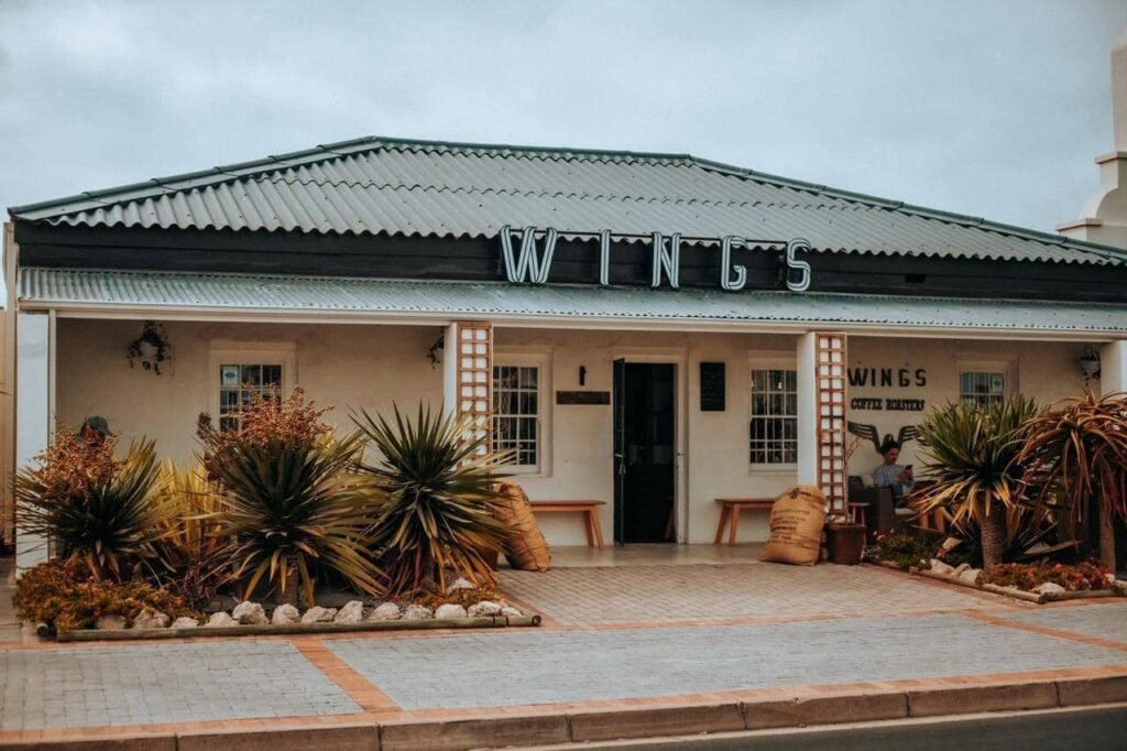 The entrance to Wings Coffee Roasters in Langebaan, with signage on the front roof, landscape garden and pillars in stone finishing.