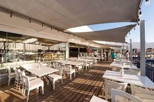 Outside deck of the Cape Town Fishmarket Restaurant in Langebaan, with wooden floor, white tables and chairs and white shade sails on poles on the marina at Club Mykonos.