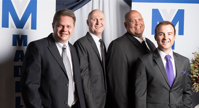 The four attorneys at Medeleyn Attorneys in langebaan with black suits and promotional material at the back of them.