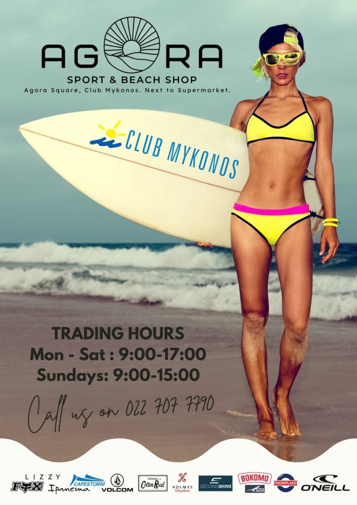 A lady walks along the beach at Langebaan with a surfboard in her hand with the words of Club Mykonos on it. She has on a bright yellow bikini that she bought from Agora Sport & Beach Shop with matching eyewear and black cap.
