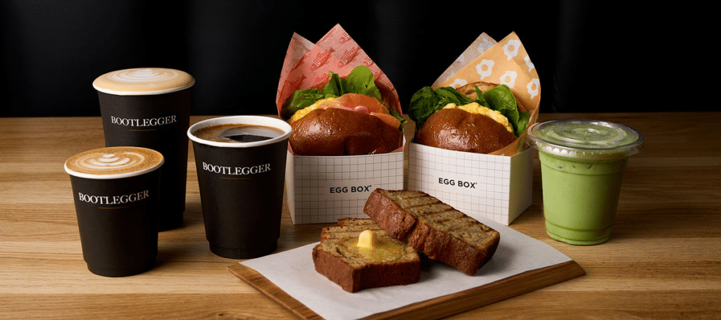 The variety available at Bootlegger Coffee Shop in Langebaan display on a table that consist of coffee in a black cup, cake and bread and egg treats .