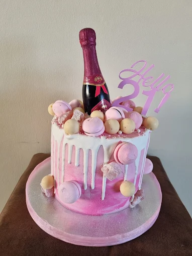 A 21 st Birthday cake with pink icing and sweets on the cake with bottle of champagne on top the cake by D-Liteful Things Catering for Cakes in Langebaan.