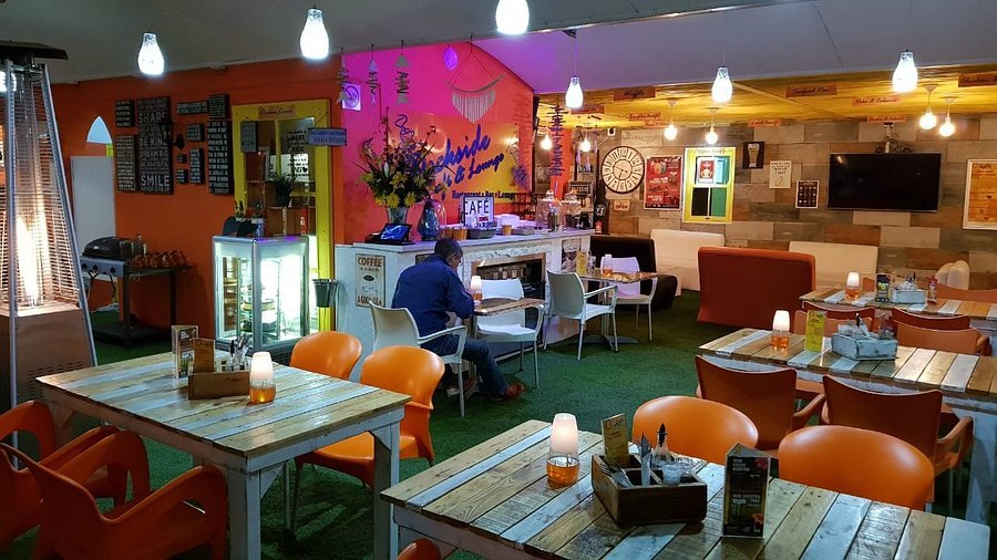 The colourful innterior of the Dockside Cafe & Lounge in Langebaan with bright walls, white tables and orange chairs.