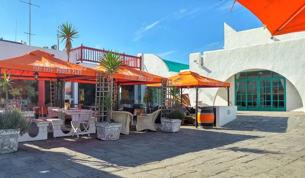 Outdoor seating at Dockside Cafe in Langebaan with white chairs and tables, orange umbrellas and the background of white buildings at Club Mykonos.