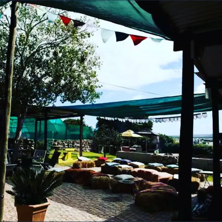 Outside seating area under green shade among trees and flags at FRIENDS Bar in Langebaan.
