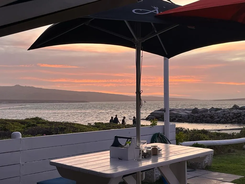 The sunset from Friday Island Beachfront Restaurant in Langebaan with white table , black umbrella and sunset over Langebaan Lagoon in a distance.