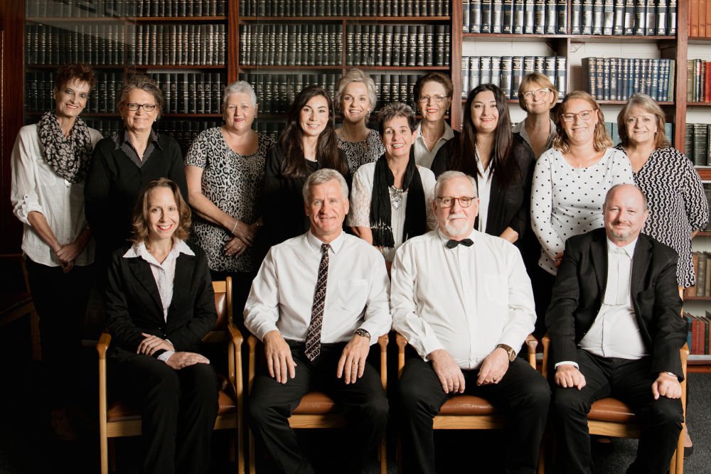 Th staff and attorneys at Gendenhuys and Jonker Attorneys in Langebaan, in a group picture infront of bookshelves full of legal books.