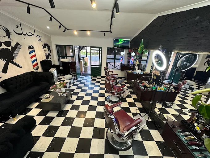 The interior of Gold Comb Barber Shop in Langebaan with balck and white floor tiles, red brber chairs and black walls with lots of mirrors against white ceiling.