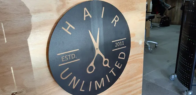 The logo of hair Unlimted Hair salon in Langebaan with wooden background and design in the shape of a watch with letters and graphics in gold on black background.
