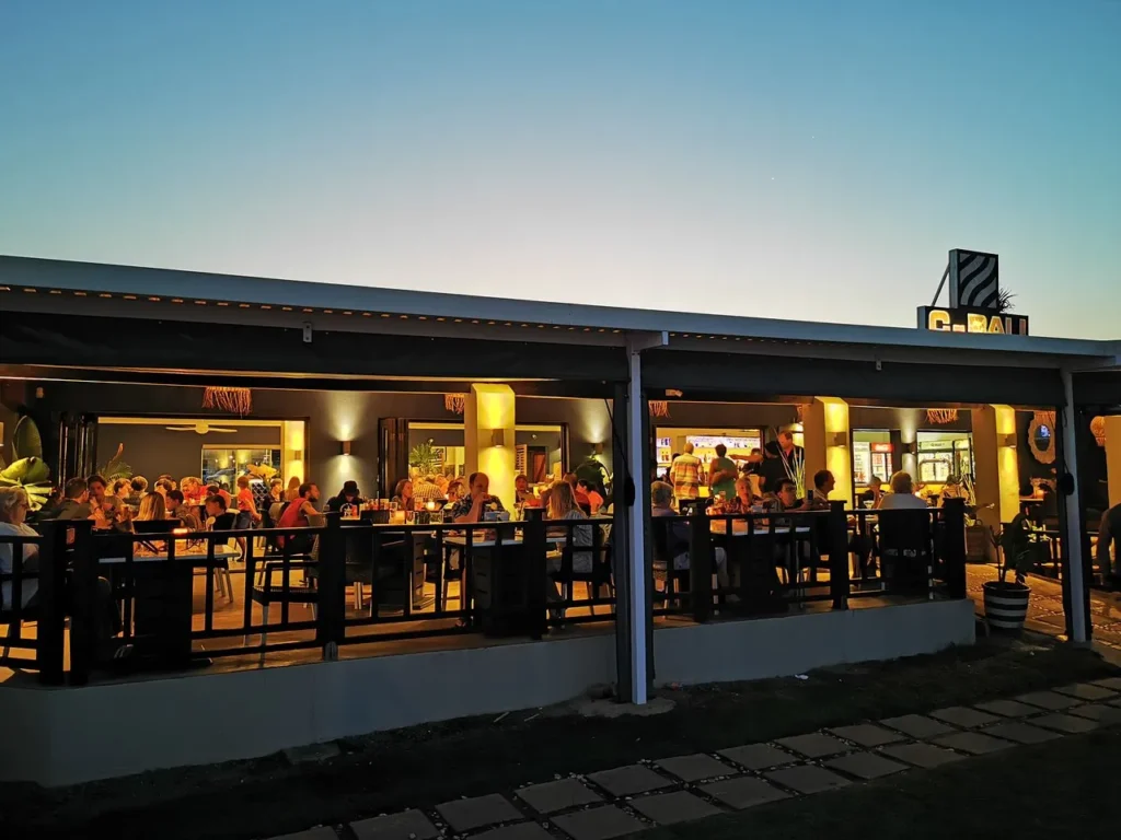Kokomos Restaurant in Langebaan at night with lots of people siiting at tbles inside and outside on deck with lights shining to create a beutiful setting on the beach.
