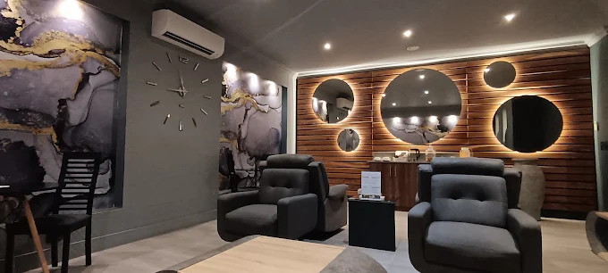 The interior of the treatment room with lots of lighted mirrors on the wall in different sizes, wooden paneling, dark chairs and grey walls.