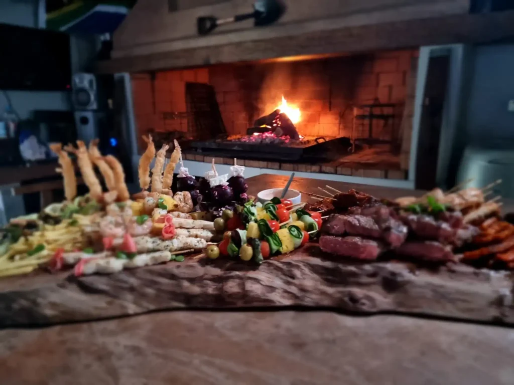A Fire in the background with variety of meat and food on display in front from Langebaan Spitbraai, Catering and Decor.