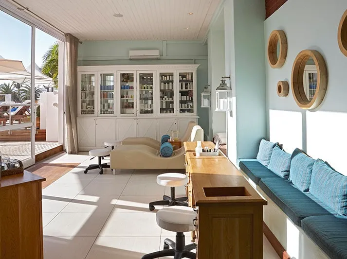 The soft looking interior of the Mint Wellness Spa in Langebaan with light blue colour seating, light blue walls, wooden furniture and white display cabinet against the wall.
