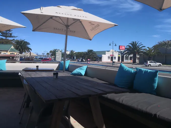 Teal cushions on seating area under white umbrella on the outside deck of the Breeze Restaurant in Langebaan with a view onto Bree Street.