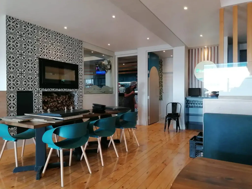 The interior of restaurant Pearly's in Langebaan with wooden floors, white walls and ceilings , wooden tables with teal colour chairs.