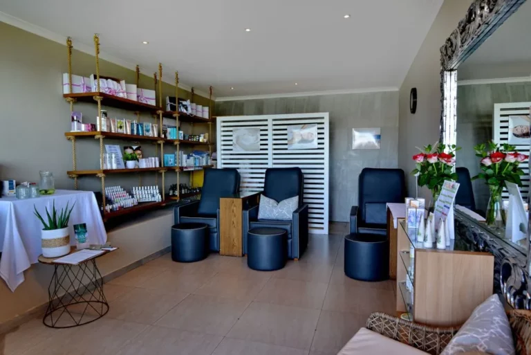 The interior of the Shark Bay Hotel Spa in Langebaan with 3 blue treatment chairs, lots of products on display on wooden shelves, free standing furniture and white background space divider.