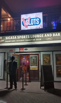 The entrance to SiCasa Sports Lounge & Bar in Langebaan at night with signage in white above the main entrance with security guard to the premises.