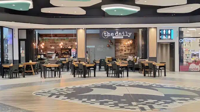 Display of tables and chairs outside The Daily Cafe Coffee Shop in Laguna Mall, Langebaan with detail tile design of the mall and signage against colourful ceiling.