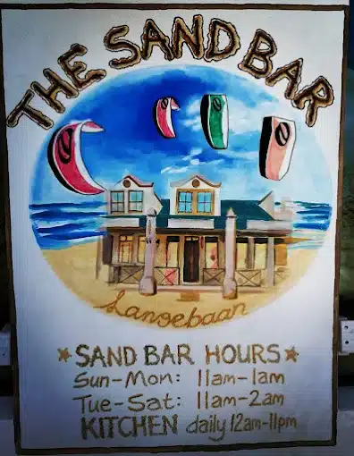 A colourful drawing of the Sand Bar in Langebaan with sea background, kite surfers aond trading hours on this board.