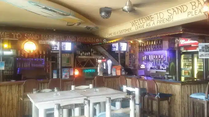 The bar counter at The sand Bar in Langebaan with lots of wood in counter and bar chairs, white seating tables and surfer boards on the ceiling to create a vibe at this local pub.