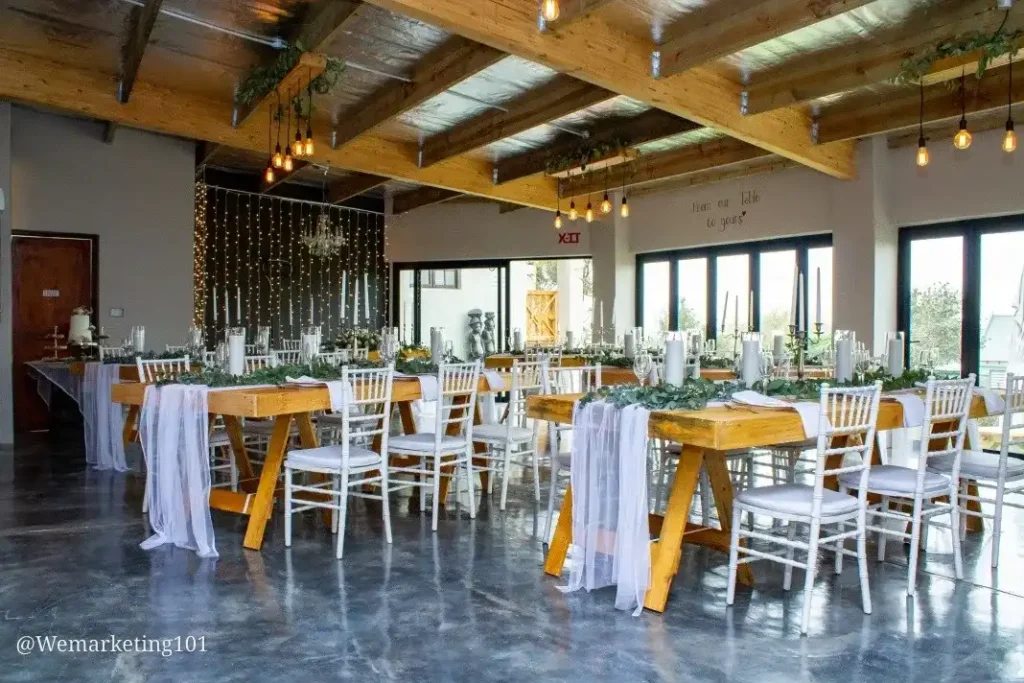 The Table as avenue for a wedding in Langebaan, Wooden tables and chairs, white and green sdecorations on table with fairy lights in the background.