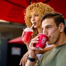 Two people drinking and sipping with a straw on their coffee at Vida e Caffee in Langebaan with red background.