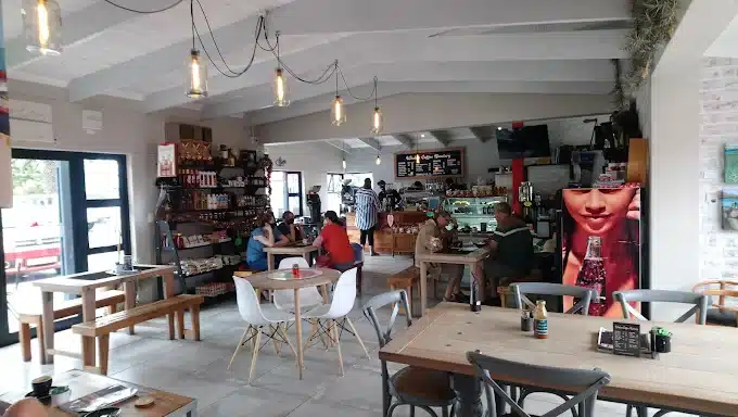 The interior of the Weskus Coffee Roastery in Langebaan with clients sitting at wooden tables with different coloured hairs and the layout of the whole store visible.
