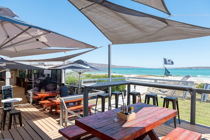 The outside decck from Wunderbar Langebaan, covered with sails for protection, wooden tables and a view towards the lagoon.