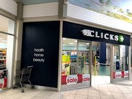 The shop front of the Clicks Pharmacy in Langebaan inside laguna Mall with blue linted windows , merchandise visible inside the store and branding in white letters on the outside.